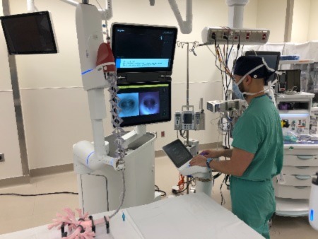 man in green scrubs controlling robotic surgery instrument while looking at video screen