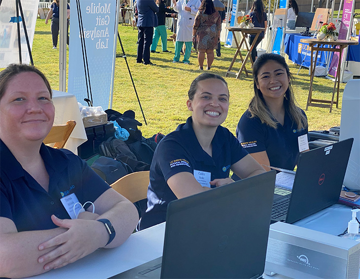 Three member of the BRaINlab team behind a desk in an athletic field event