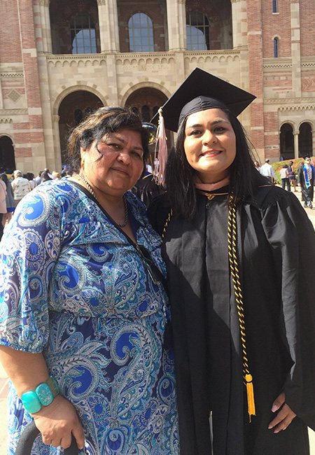 Jacqueline León, in black graduation cap and gown, stands with her mother in front of brick building at UCLA