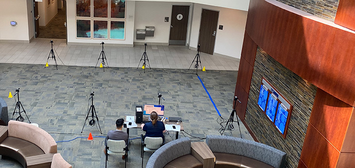 The lobby area showing eight cameras on tripods set to detect motion and two individuals sitting next to a desk with a computer and monitor.