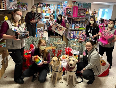 Eight people and two facility dogs pose in storeroom filled with toy donations