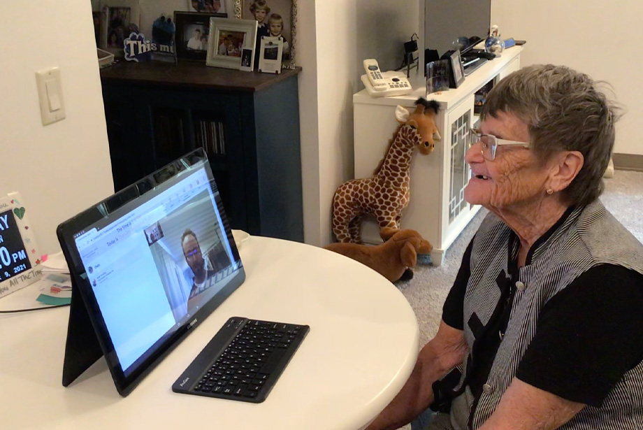 Older woman sits at kitchen table looking at man on computer screen