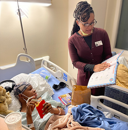 Darren in his hospital bed with Karen standing helping with homework