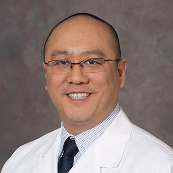 Asian American doctor smiling into camera with glasses and dressed in white coat