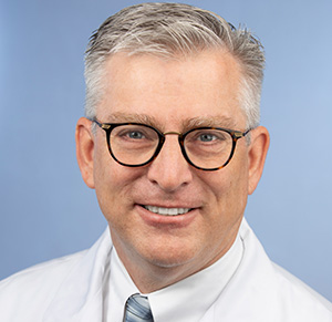a middle-aged doctor with short whitish-gray hair, wearing eyeglasses and a white coat