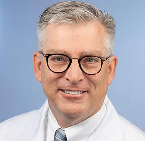 middle-aged doctor with short whitish-gray hair, glasses and a white coat