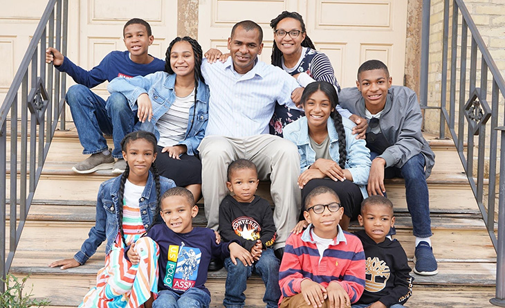 Darren with his parents and eight siblings sitting on stairs in front of a house