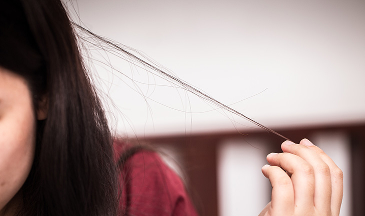 A teenage girl with long dark hair pulls on a strand of her hair. Only the side of her head is visible.