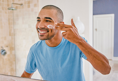 Man applying moisturizer to his face in front of the mirror