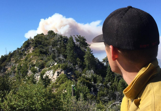  Firefighter looks at smoke over mountain in the distance