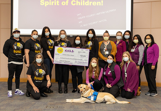 Fifteen Spirit Halloween and Child Life team members and a dog gather with large check. 