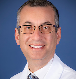 Man with graying hair and glasses in a white lab coat on blue background