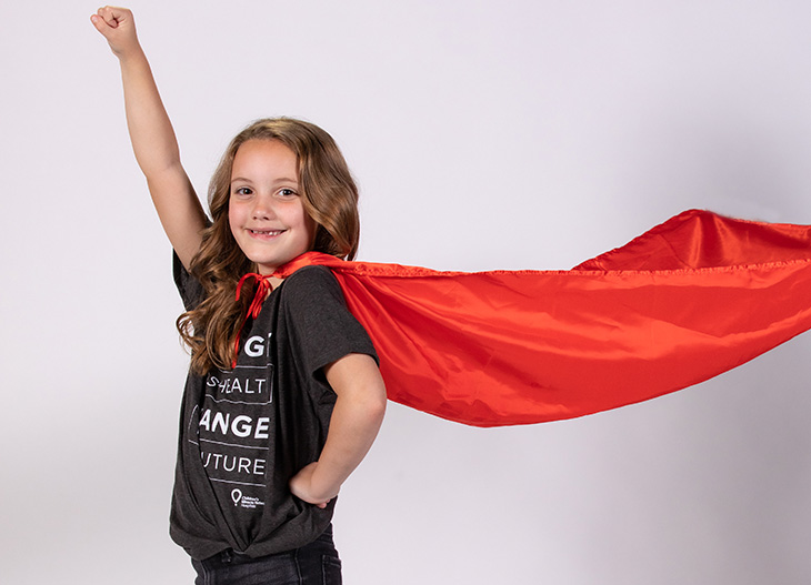 young girl wearing a red cape that is flying in the air