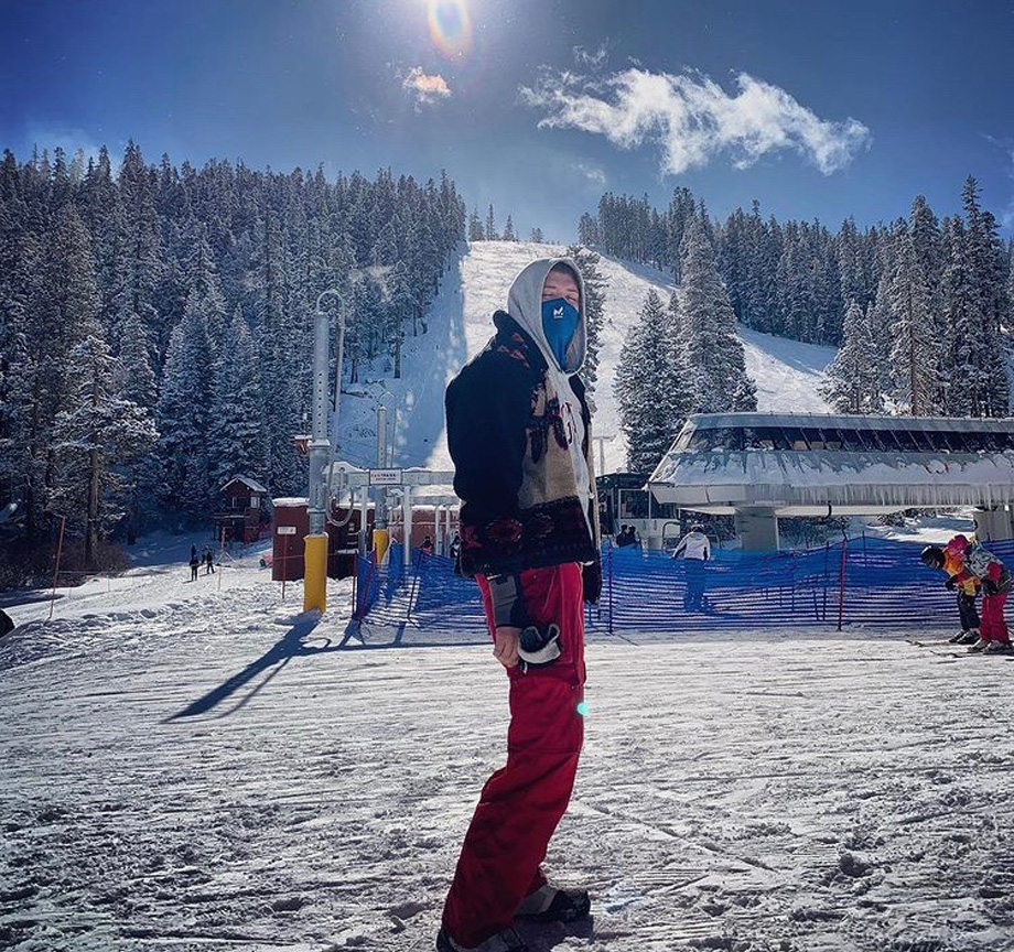 Jake Brazier stands in front of ski slope wearing ski gear and holding ski goggles