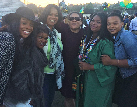 Chelsea Nash in green graduation gown poses with friends at her Castro Valley High School graduation with balloons in background