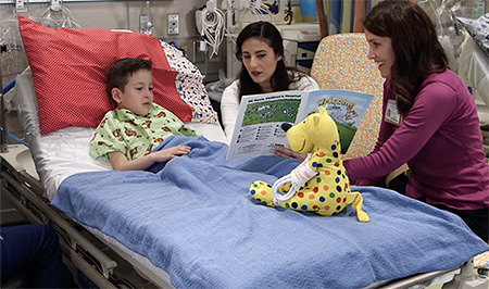 Child in a hospital bed with two adults reading a book