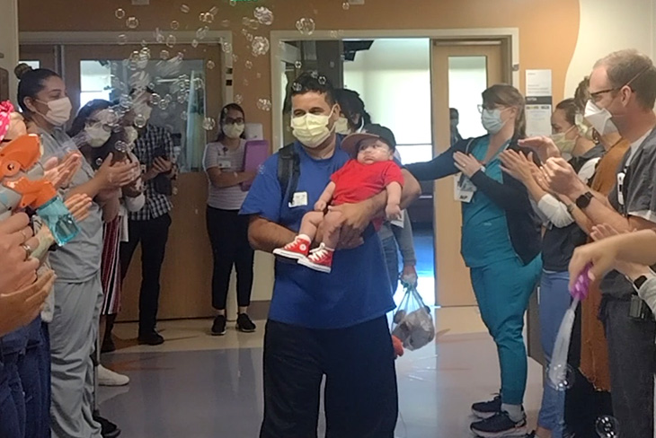 Baby patient leaving the hospital with parents and staff lining the hallway bubbles in the air