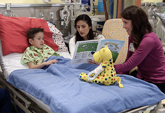 Child in a hospital bed with two adults reading a book