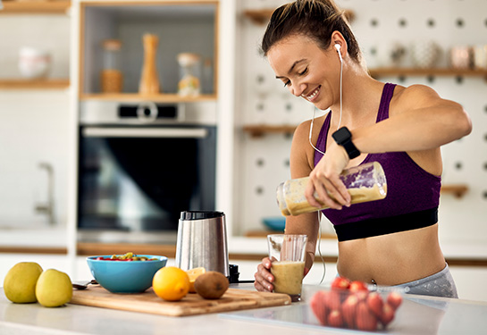 Sportswoman in workout clothes pouring a fruit smoothie in the kitchen