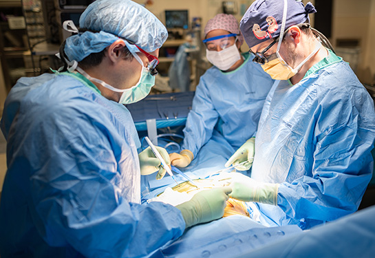 Three doctors in scrubs performing surgery