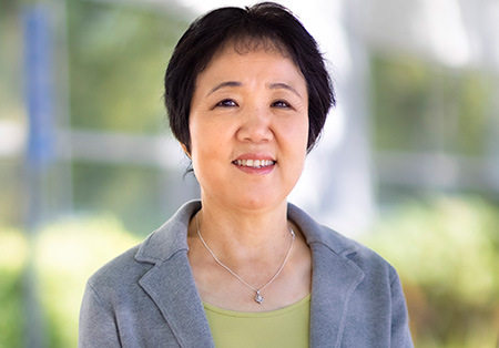 Asian American woman with short, dark hair standing with hands crossed and smiling.