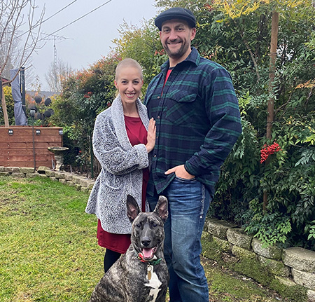 Man and woman with grey and black dog in front of large tree