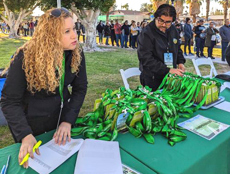 A woman holds down a white piece of paper on a table with a pile of name tags with green lanyards. 
