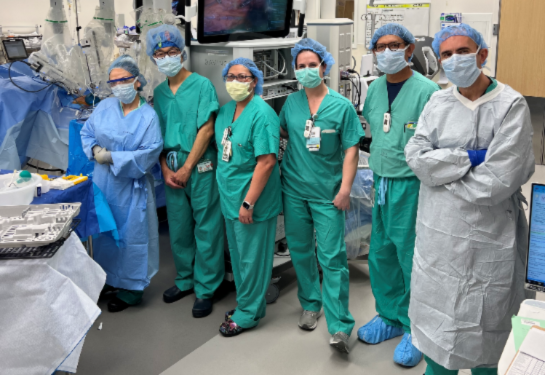 Five people posing in surgical room wearing green scrubs