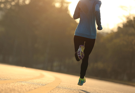 Young fitness woman runner running on a road at sunrise