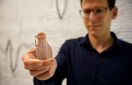 Man with brown hair and navy long sleeve shirt holds a rectangular plastic slide which in turn holds a small square probe.