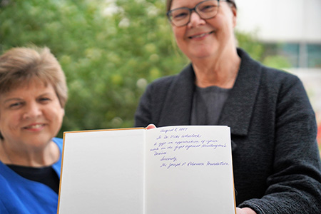 Two women holding an open book, displaying the inscribed inner pages.