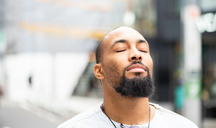 An African American man stands outside with his eyes close, face tilted up to the sun