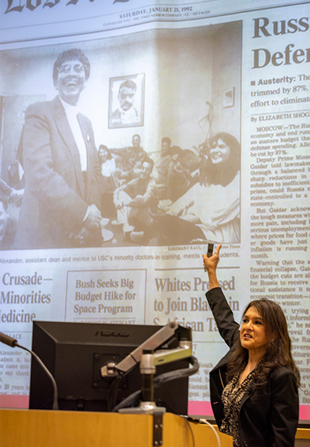 Surgeon General Diana Ramos stands at podium in front of a large screen with a Los Angeles Times front page photo that shows her image