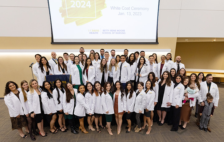 A group of 43 smiling nursing students pose with celebratory hand gestures during their pinning ceremony