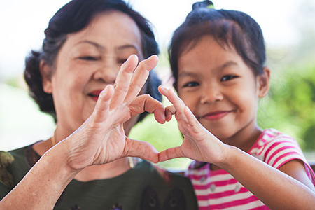 Older woman and younger child form a heart symbol with both hands
