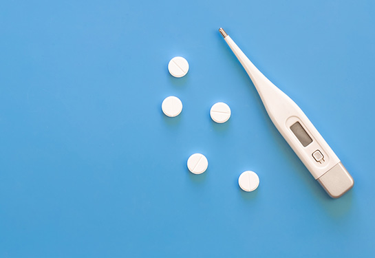 a digital thermometer and five white pills are shown on a blue background. 