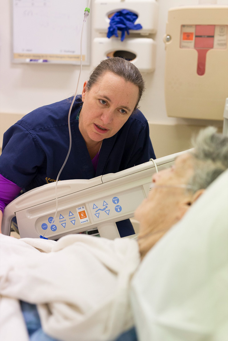 Physician speaks to older patient lying in emergency department bed