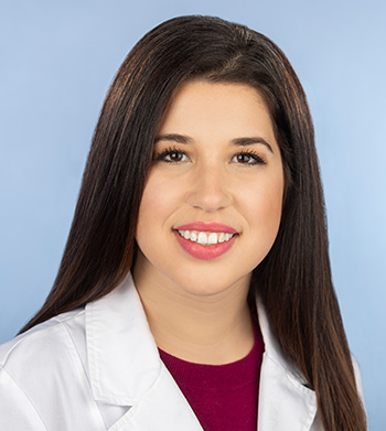 Woman smiling into camera pictured above the shoulders with dark hair wearing white doctor coat.