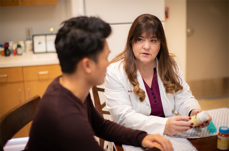 Nursing instructor, right, looks at student while sitting at table holding a prescription bottle