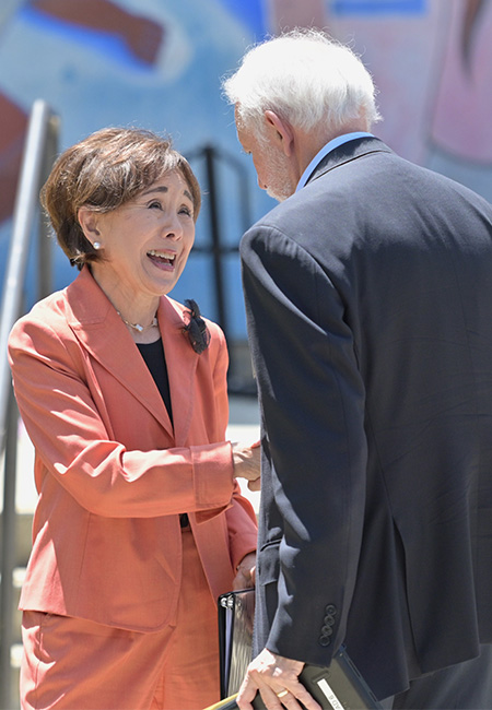 Woman with dark hair and orange suit, on left, smiles at a man wearing blue suit and gray hair