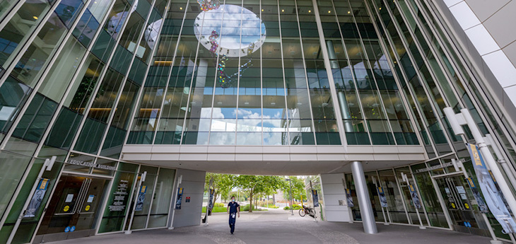Building with glass windows and person wearing blue scrubs walking in front of the building