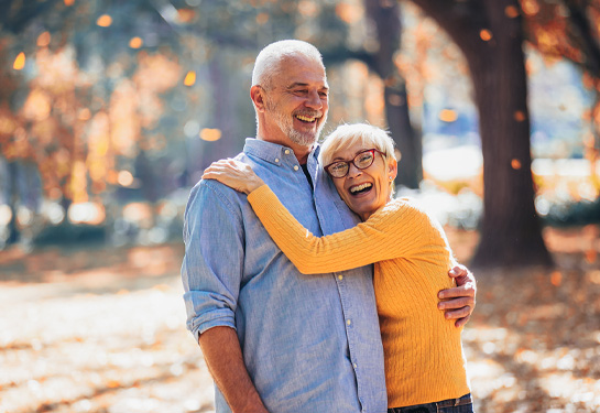 Older white couple embraces outdoors amid falling leaves