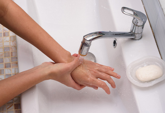 person&#x2019;s hands above sink with water running from faucet over them
