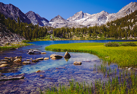 Blue sky moutains behind rocky water and grass
