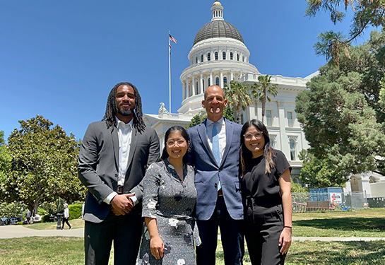 Three medical students pose with state lawmaker wearing blue suit outside the Capitol Building in Sacramento 