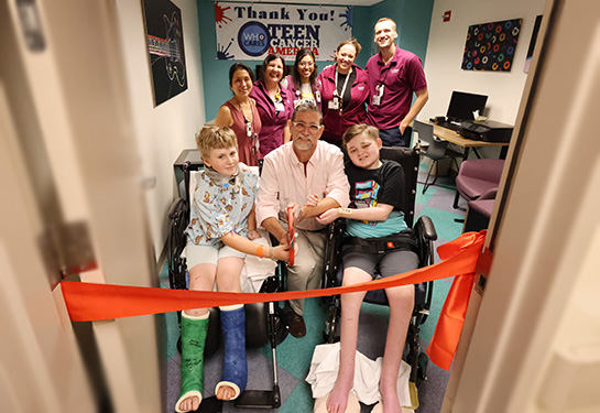 Physician, two patients and a group of medical staff at the ribbon cutting for the teen cancer lounge