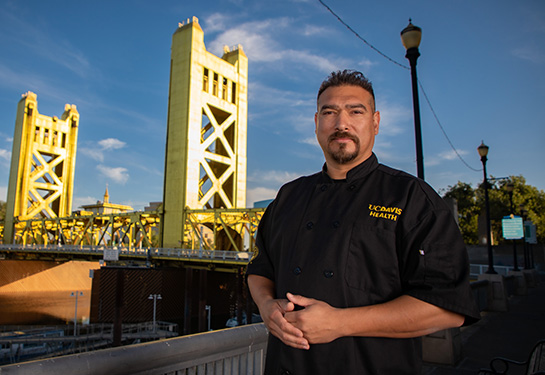 Santana Diaz wearing black chef coat standing in front of golden bridge