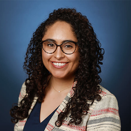 Portrait of woman wearing glasses and with dark, curly hair past her shoulders.