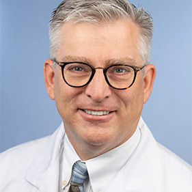 Man with graying hair and glasses wearing a white lab coat.