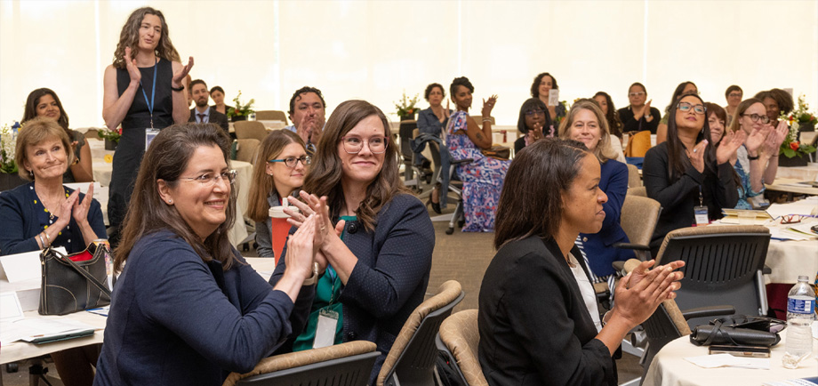 People sitting at or standing at tables clapping and smiling.